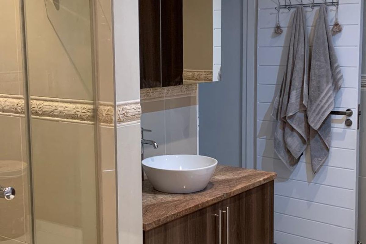 A modern bathroom featuring a glass-enclosed shower, a vanity with a stone countertop, a vessel sink, and tiled walls.