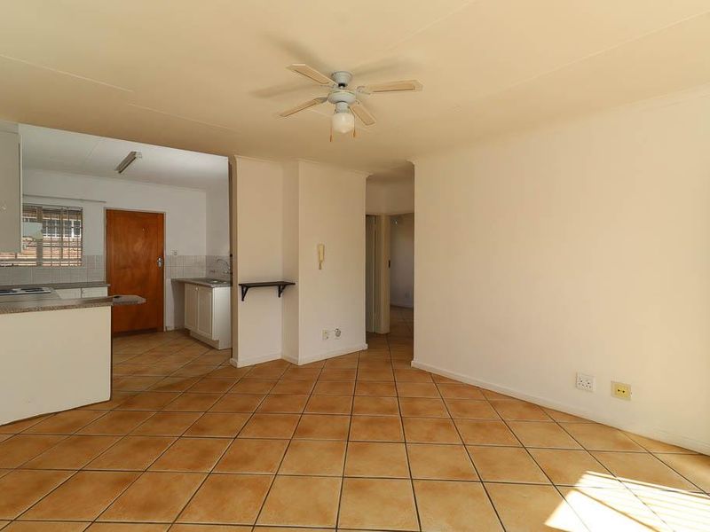 An open-plan living and kitchen area featuring tiled flooring, a ceiling fan, and functional kitchen cabinetry with built-in appliances.