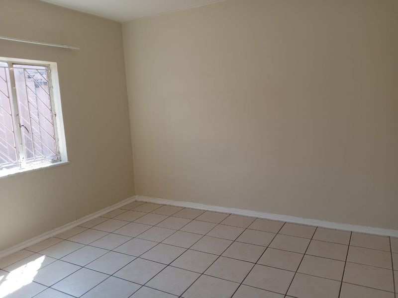 A vacant bedroom featuring neutral wall paint, tiled flooring, and a window fitted with security bars.