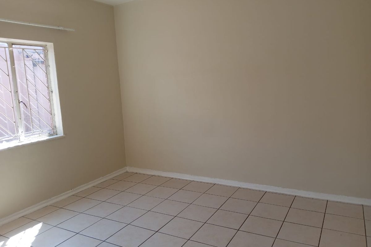 A vacant bedroom featuring neutral wall paint, tiled flooring, and a window fitted with security bars.