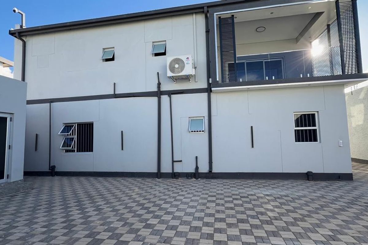 Rear elevation of a modern two-story house featuring a paved courtyard, balcony, and external air conditioning unit.
