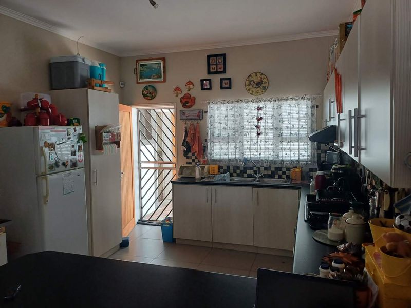 Functional kitchen featuring built-in cabinetry, double sink, tiled splashback, and direct access to an exterior security gate.