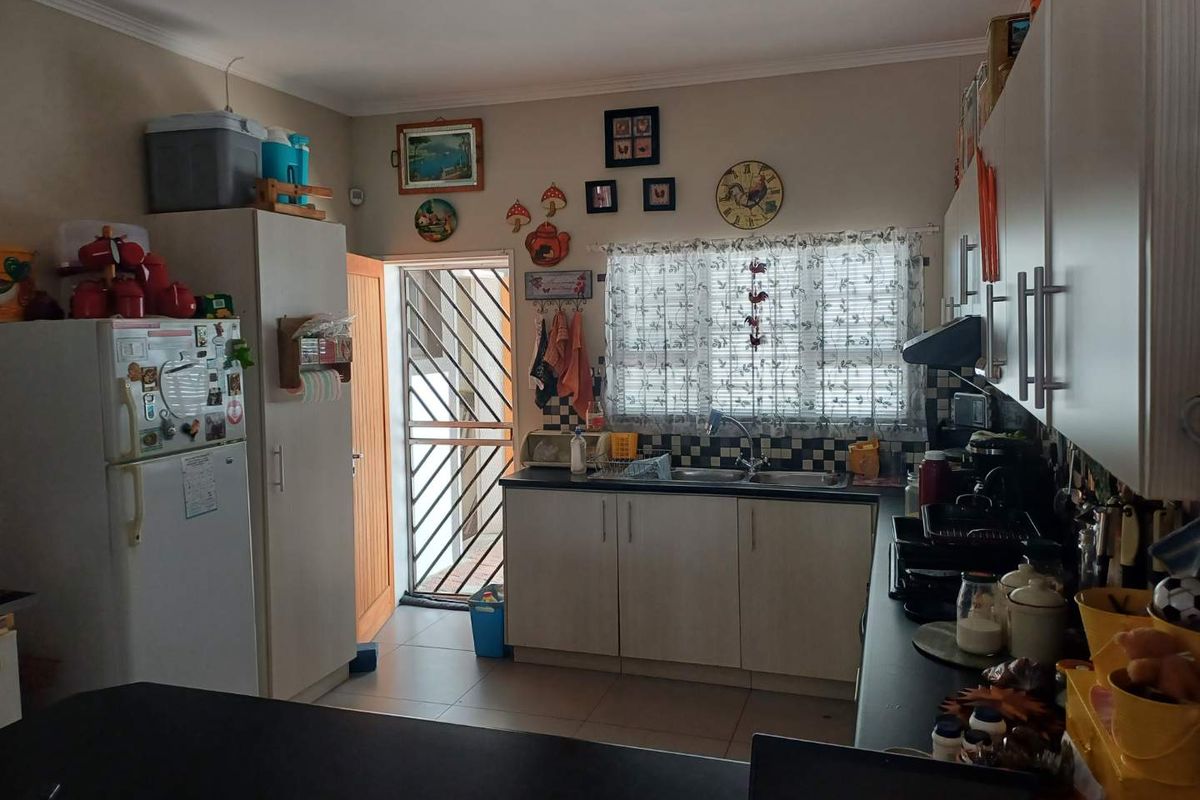 Functional kitchen featuring built-in cabinetry, double sink, tiled splashback, and direct access to an exterior security gate.
