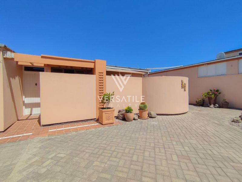 A well-maintained front entrance area featuring a paved driveway, curved masonry wall, and a covered pergola entrance.
