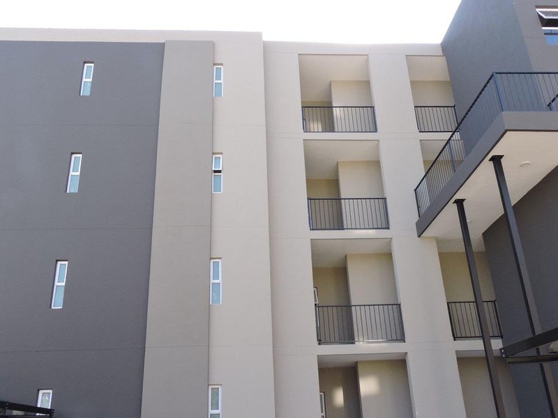 A modern apartment building exterior featuring a multi-toned facade, private balconies with metal railings, and contemporary casement windows.