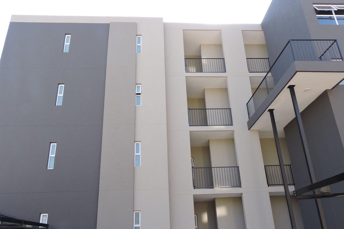 A modern apartment building exterior featuring a multi-toned facade, private balconies with metal railings, and contemporary casement windows.