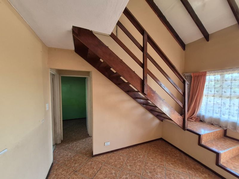 An open living area featuring a wooden staircase, exposed ceiling beams, and tiled flooring, offering a blank canvas for renovation and modernization.