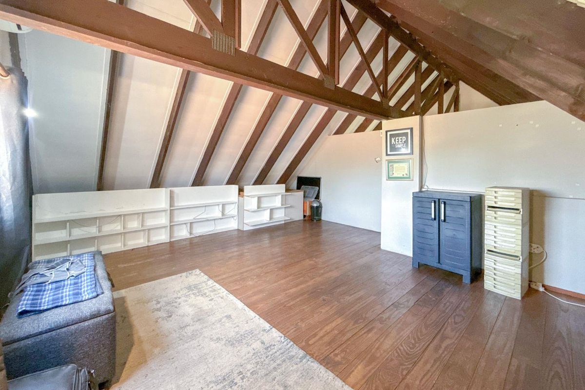 Spacious attic-style bedroom featuring exposed timber roof trusses, wooden flooring, and built-in low-level shelving units.