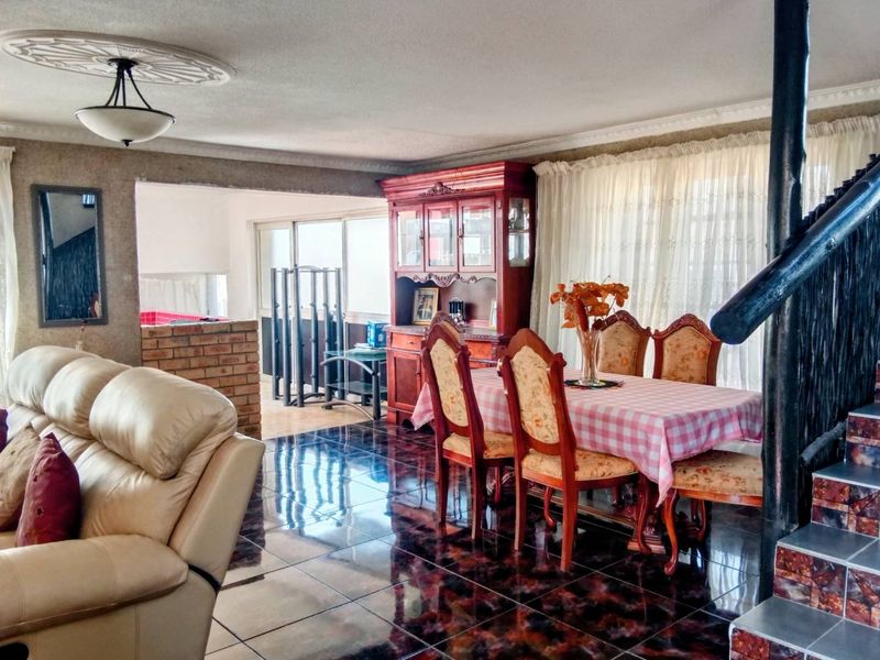 Open plan living and dining area featuring dark tiled flooring, a decorative ceiling rose, and a brick partition leading to an adjacent space.