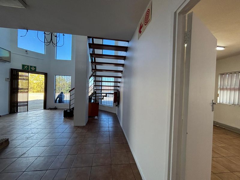 Spacious industrial entrance hall featuring tiled flooring, an open-tread staircase, and large windows providing natural light.