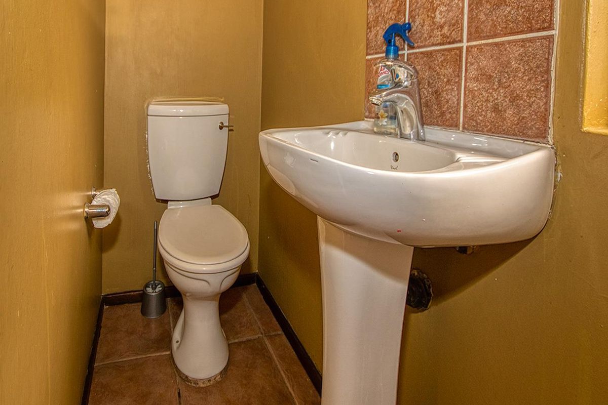 A compact guest bathroom featuring a white pedestal basin with tiled splashback and a standard toilet.