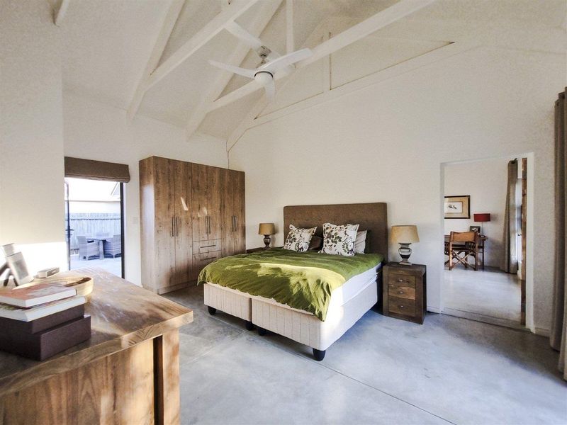 Spacious bedroom featuring a vaulted ceiling with a fan, polished concrete flooring, and built-in cabinetry, with direct access to an outdoor patio area.