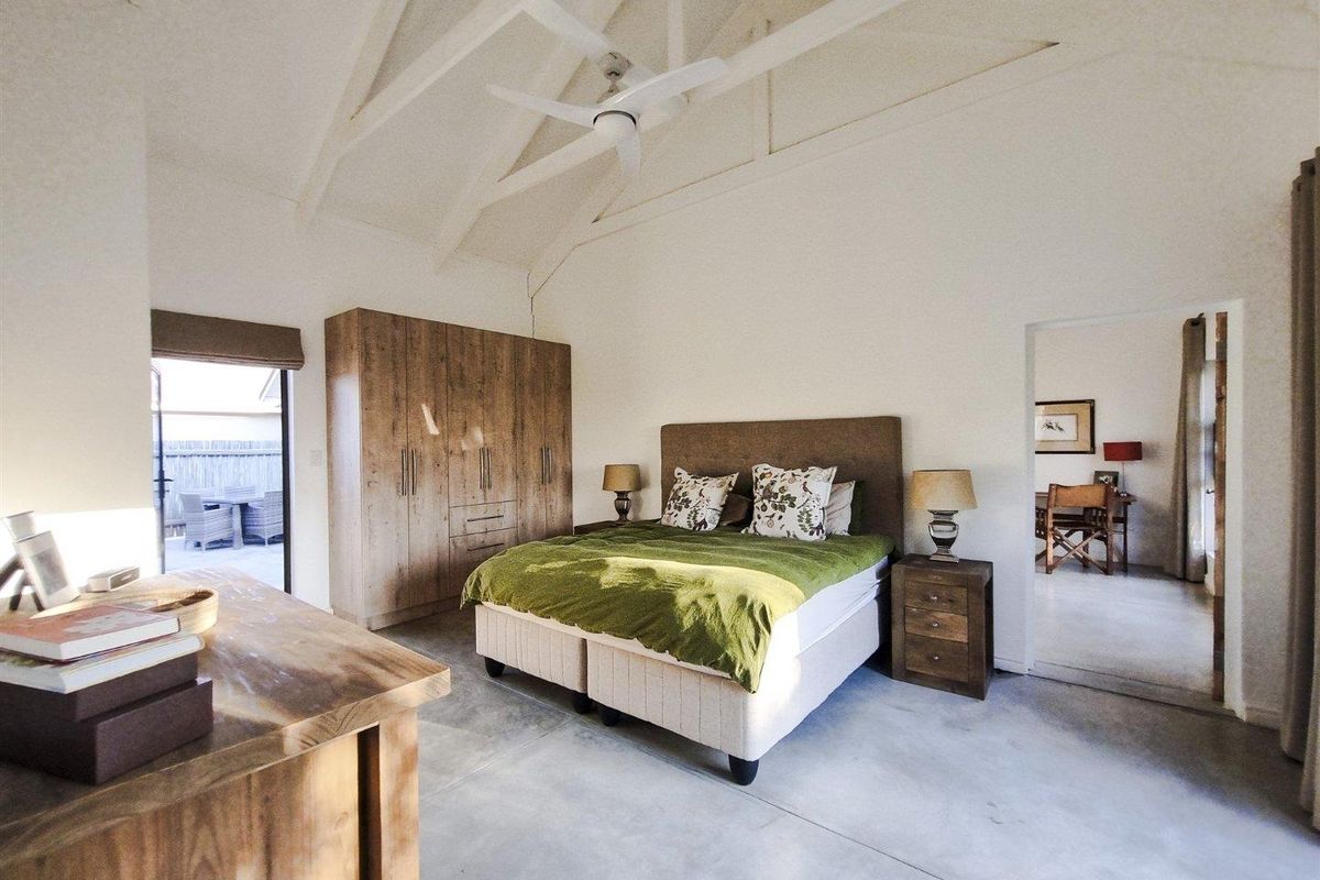 Spacious bedroom featuring a vaulted ceiling with a fan, polished concrete flooring, and built-in cabinetry, with direct access to an outdoor patio area.