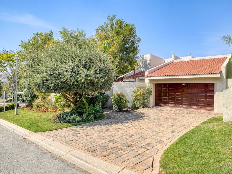 Front exterior view of the property featuring a paved driveway, a single garage door, and a well-maintained garden area.