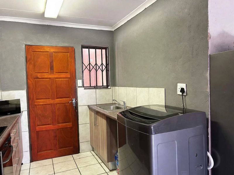 A functional laundry area featuring a stainless steel sink, tiled splashback, and built-in cabinetry, providing essential utility space for the apartment.