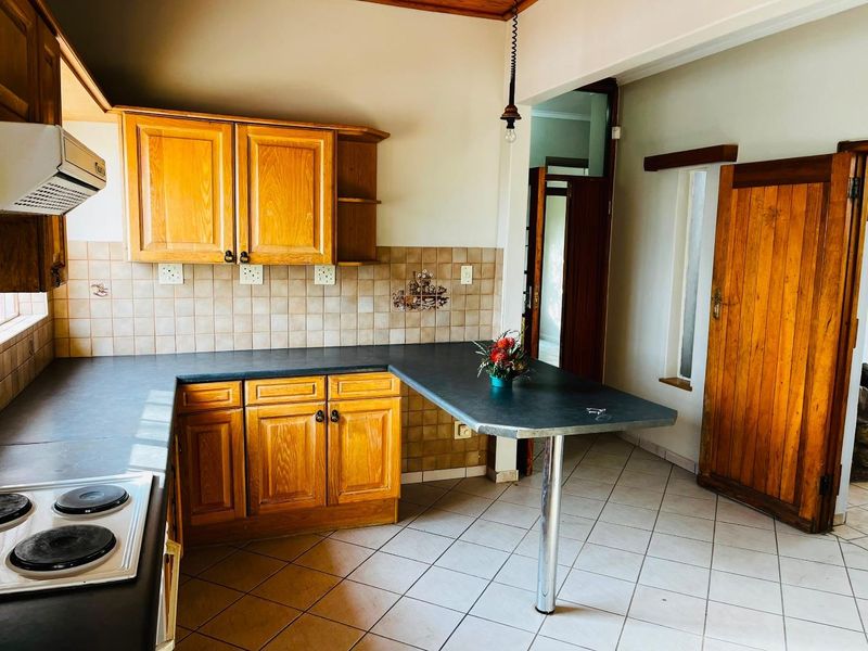 A functional kitchen featuring wooden cabinetry, a breakfast bar, ceramic tile flooring, and a built-in electric hob with an extractor fan.
