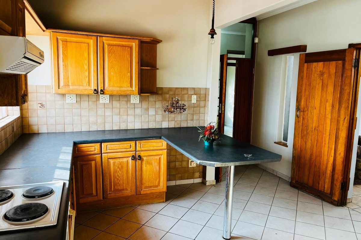 A functional kitchen featuring wooden cabinetry, a breakfast bar, ceramic tile flooring, and a built-in electric hob with an extractor fan.