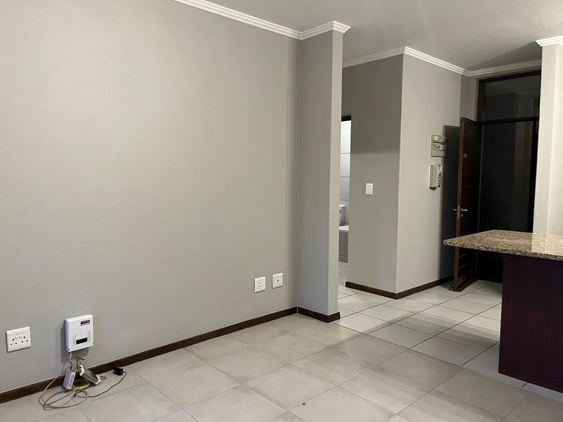 An open-plan living area featuring neutral grey walls, tiled flooring, and a granite breakfast counter, providing a clean and versatile space.