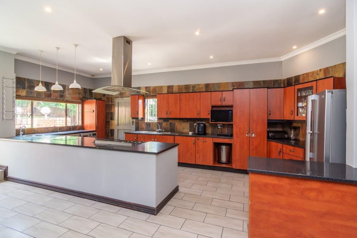 Spacious kitchen featuring wooden cabinetry, granite countertops, a central island with a gas hob, and a tiled backsplash.