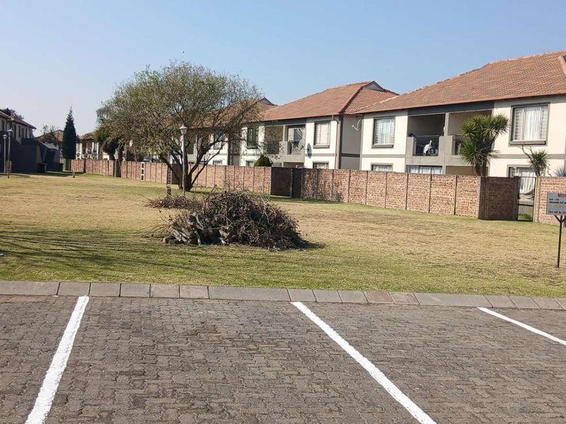View of the apartment complex exterior featuring a paved parking area, communal lawn, and brick boundary wall.