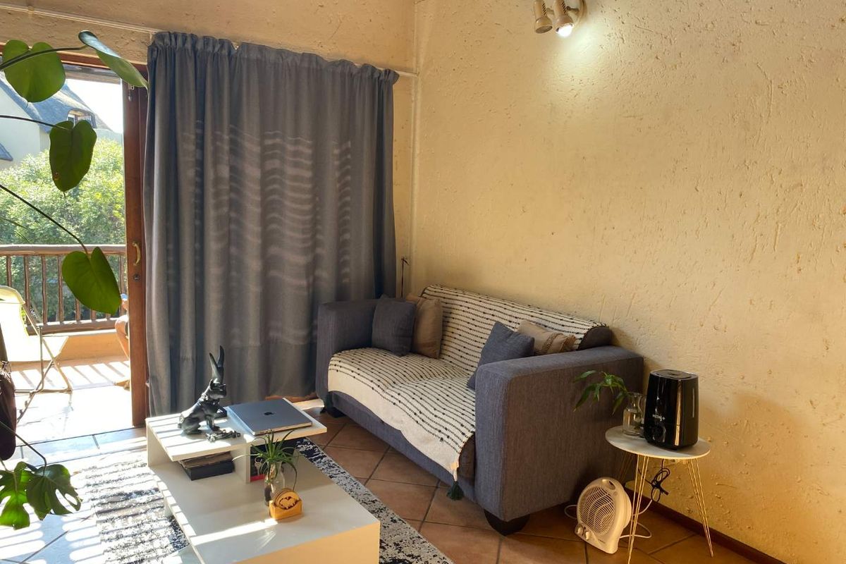 A living room featuring tiled flooring and direct access to a balcony through a sliding glass door, providing natural light and outdoor connectivity.