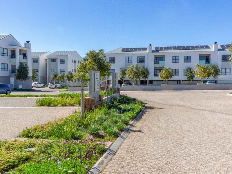 A view of the apartment complex exterior featuring paved driveways, landscaped garden beds, and buildings equipped with solar panels.