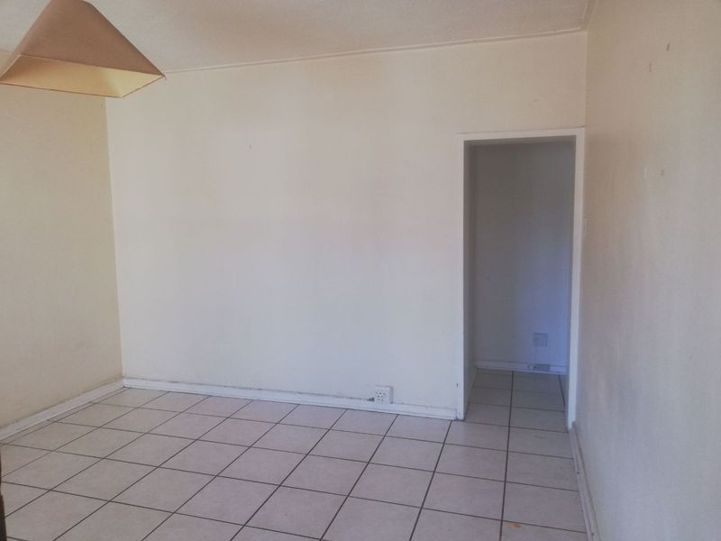 An empty living area featuring neutral ceramic floor tiles and plain walls, providing a blank canvas for interior design updates.
