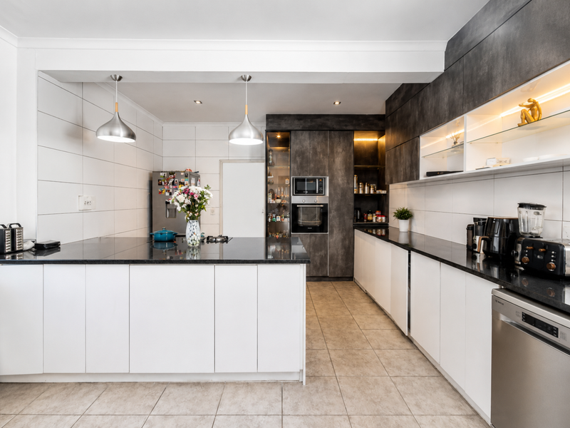Modern kitchen featuring sleek white and dark cabinetry, granite countertops, integrated appliances, and stylish pendant lighting, offering a clean and functional workspace.