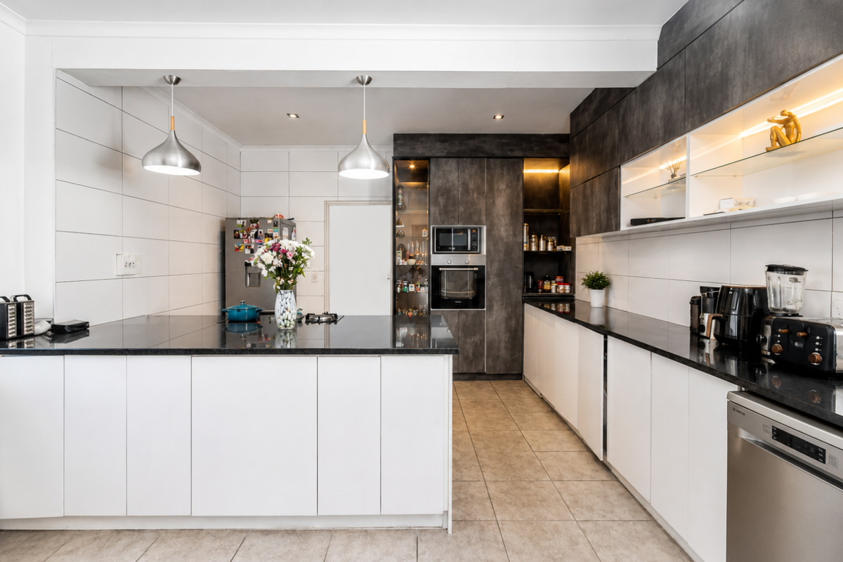 Modern kitchen featuring sleek white and dark cabinetry, granite countertops, integrated appliances, and stylish pendant lighting, offering a clean and functional workspace.