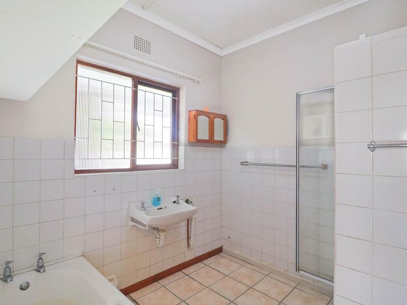 A functional bathroom featuring a bathtub, separate shower enclosure, and wall-mounted basin with tiled finishes throughout.