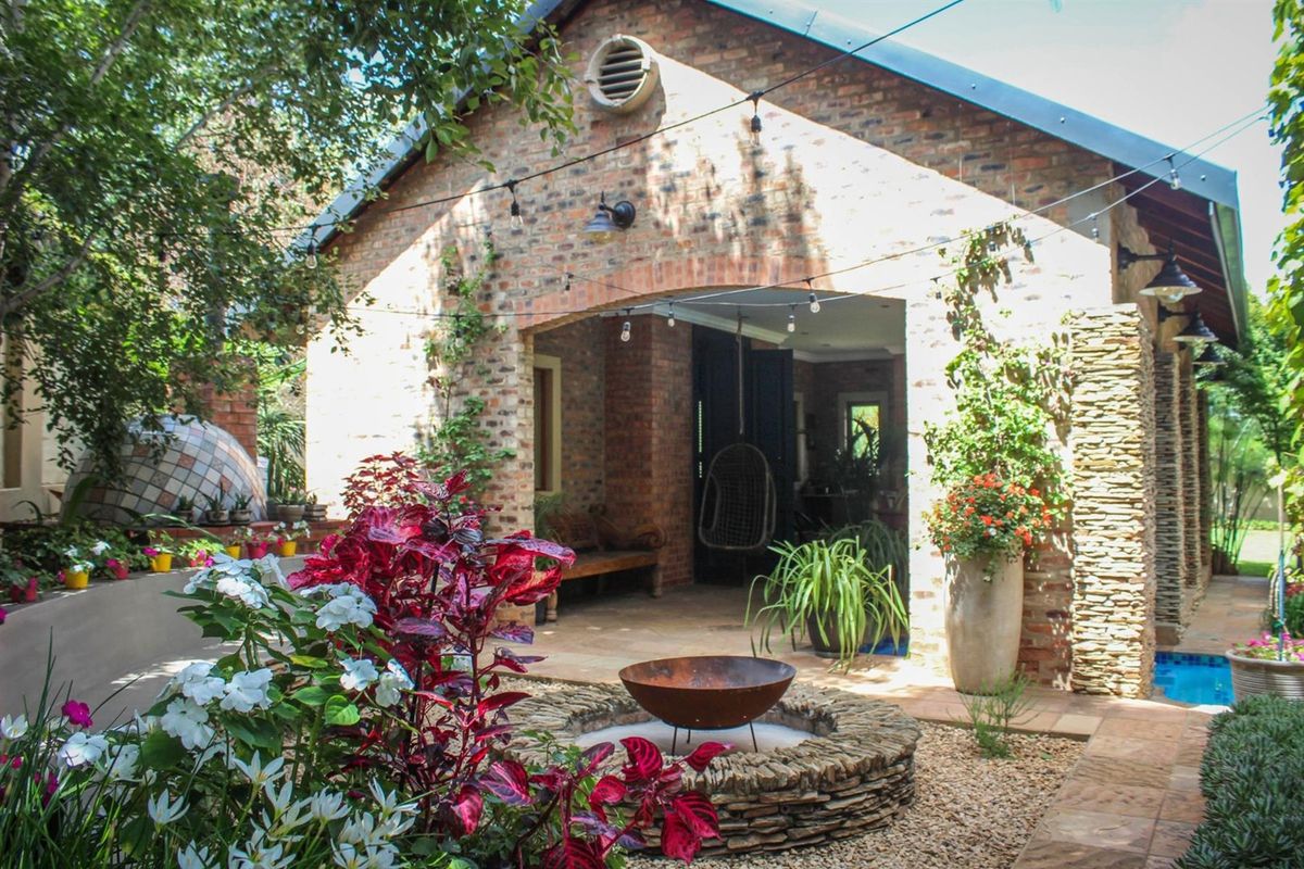 Charming rear exterior featuring an exposed brick facade, covered patio area, stone fire pit, and a built-in pizza oven set within a landscaped garden.
