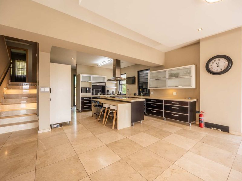 Spacious open-plan kitchen and living area featuring a central island, modern cabinetry, stone countertops, and tiled flooring, with an adjacent staircase.
