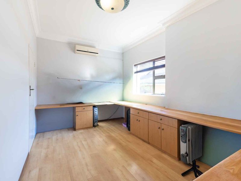 A functional home office featuring extensive built-in desk space, integrated cabinetry, laminate flooring, and a wall-mounted split-system air conditioner.