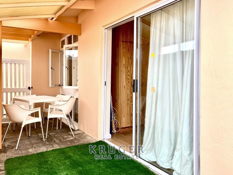 A covered patio area featuring paved flooring, artificial turf, and a sliding glass door providing access to the interior.