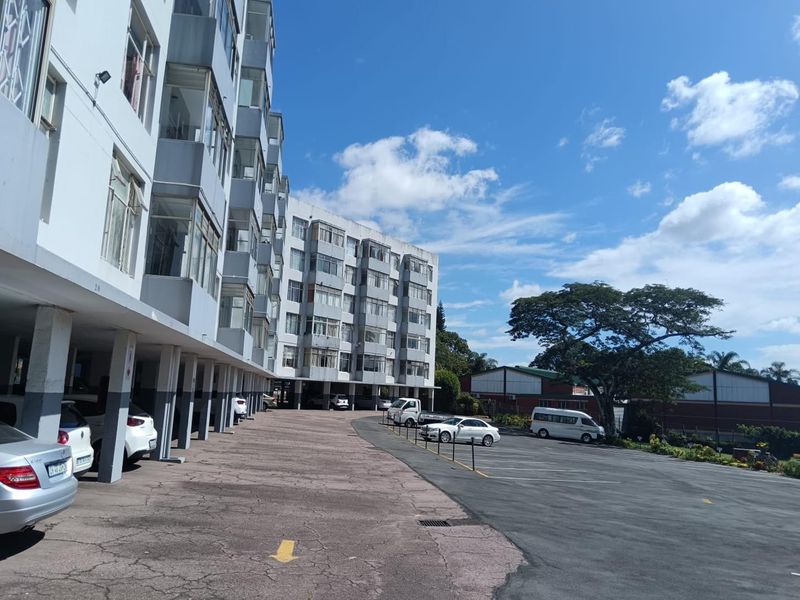 Exterior view of a multi-story townhouse complex featuring covered parking bays and an asphalt driveway area.