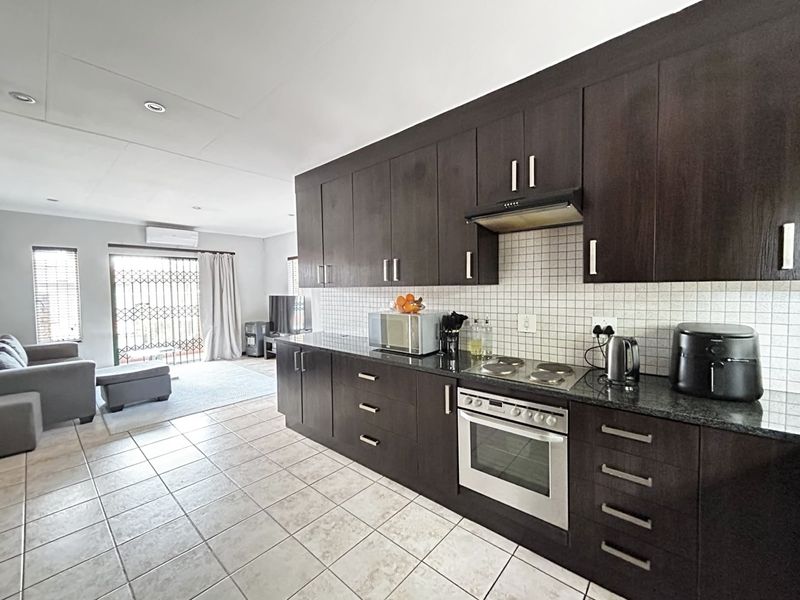 Open-plan living area featuring a modern kitchen with dark wood cabinetry, granite countertops, built-in appliances, and tiled flooring, flowing into a bright lounge space.