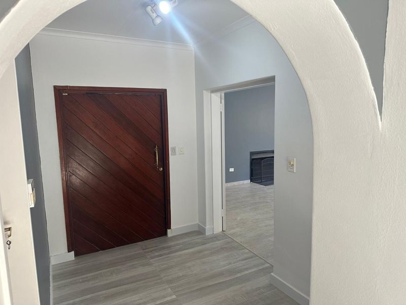An inviting entrance hall featuring a distinctive arched doorway, solid wood front door, and modern light-toned laminate flooring leading into the living area.