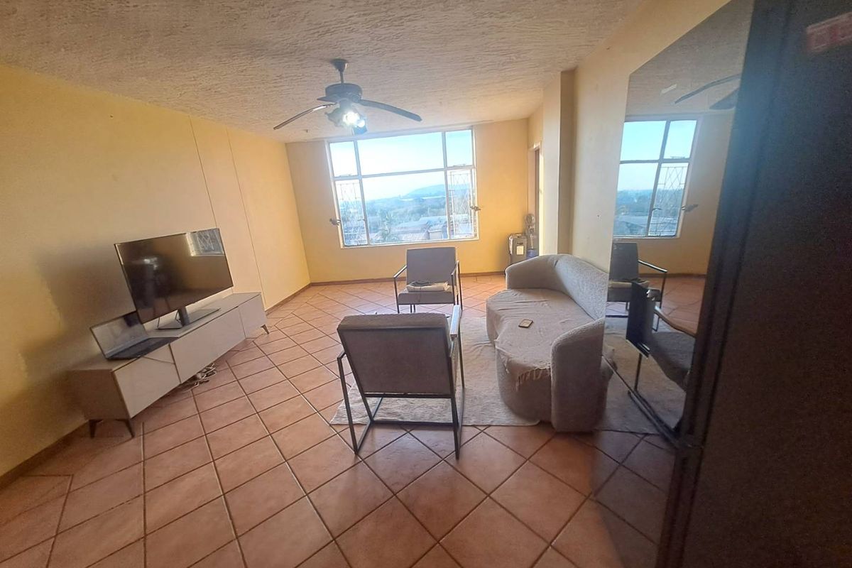 Spacious living room featuring large windows with natural light, tiled flooring, and a ceiling fan, offering a blank canvas for modern updates.