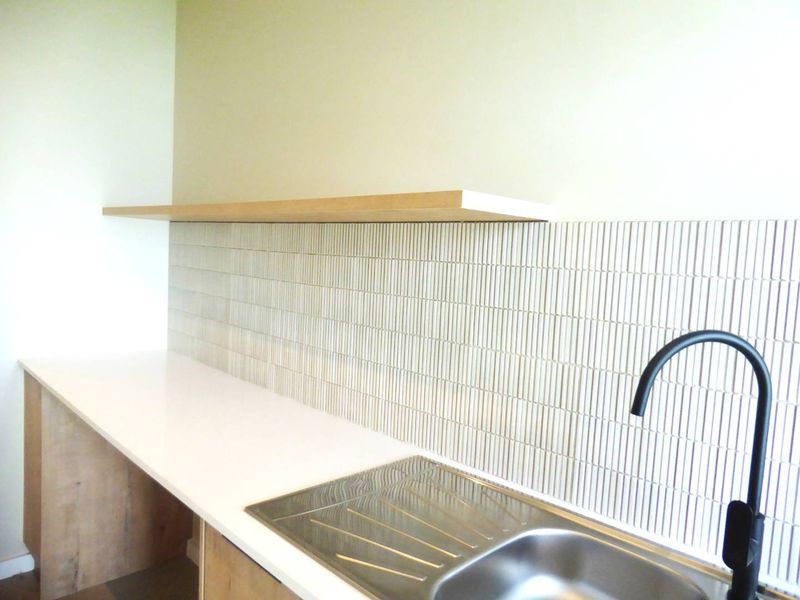 A modern kitchen area featuring a clean stone countertop, stainless steel sink with a contemporary black faucet, and stylish vertical tiled backsplash.