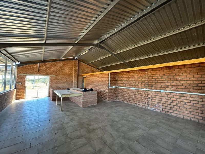 A spacious utility area featuring exposed brick walls, tiled flooring, and a corrugated metal roof, suitable for a workshop or multi-purpose storage space.