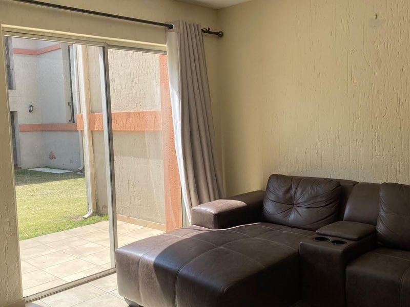 A living room featuring tiled flooring and a large sliding glass door providing direct access to an outdoor patio and garden area.