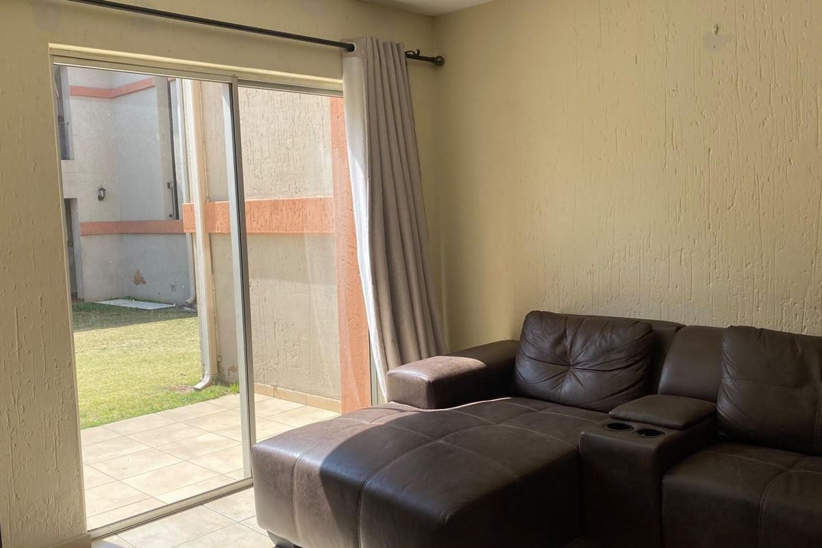 A living room featuring tiled flooring and a large sliding glass door providing direct access to an outdoor patio and garden area.