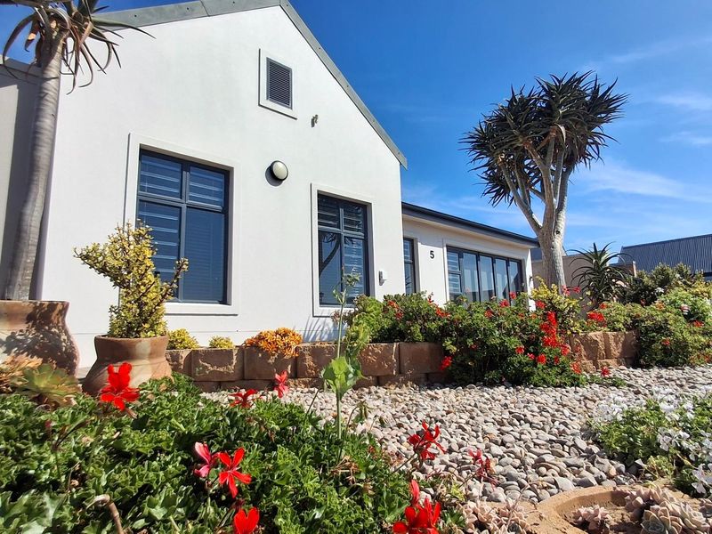 A well-maintained front facade featuring modern aluminium window frames, a landscaped pebble garden, and a stone retaining wall.