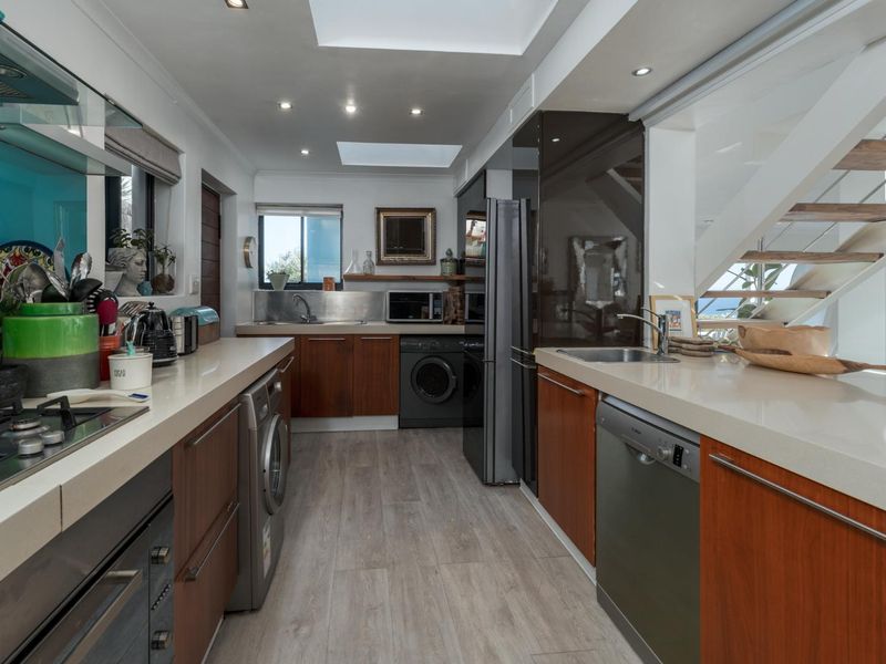 Modern galley-style kitchen featuring wood-finish cabinetry, stone countertops, integrated appliances, and dual skylights, with an adjacent staircase.