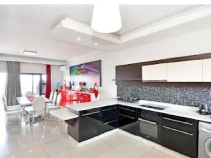 Modern open-plan kitchen and dining area featuring sleek dark cabinetry, integrated appliances, tiled flooring, and direct access to a balcony through sliding glass doors.