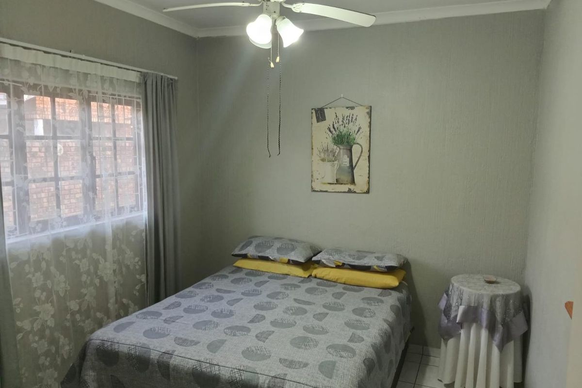 A functional bedroom featuring tiled flooring, a ceiling fan, and a window fitted with security burglar bars.