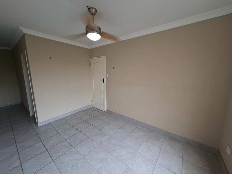An empty living area featuring neutral wall tones, tiled flooring, and a central ceiling fan, offering a blank canvas for interior design.