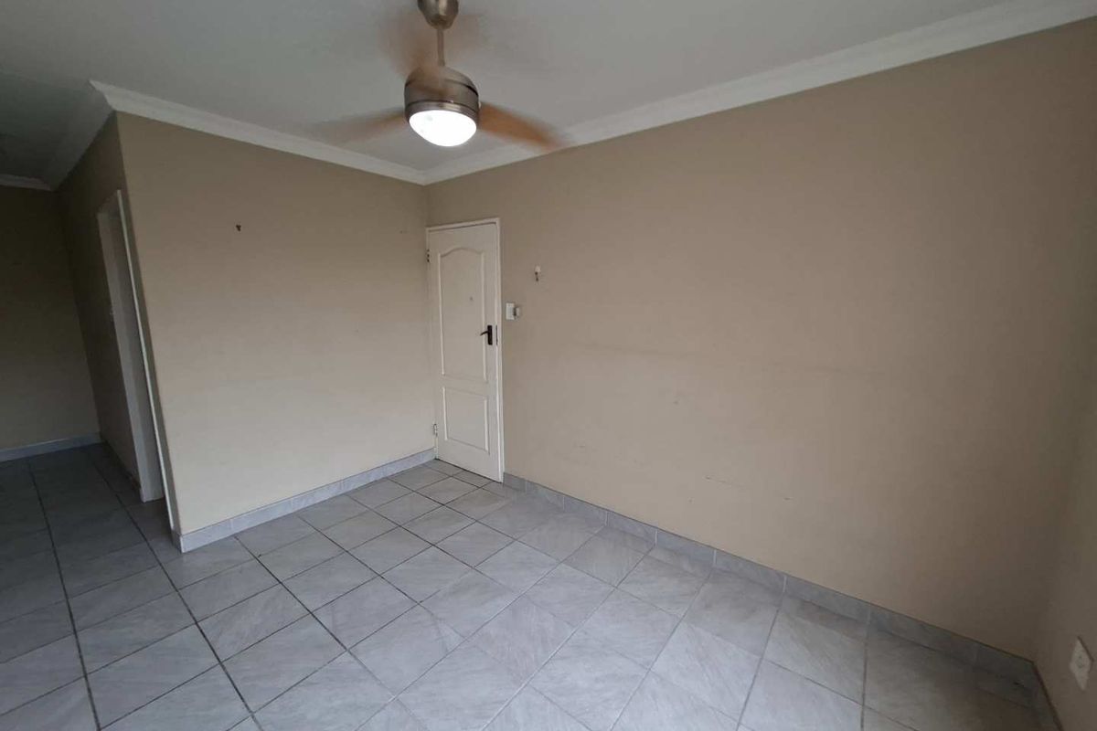 An empty living area featuring neutral wall tones, tiled flooring, and a central ceiling fan, offering a blank canvas for interior design.