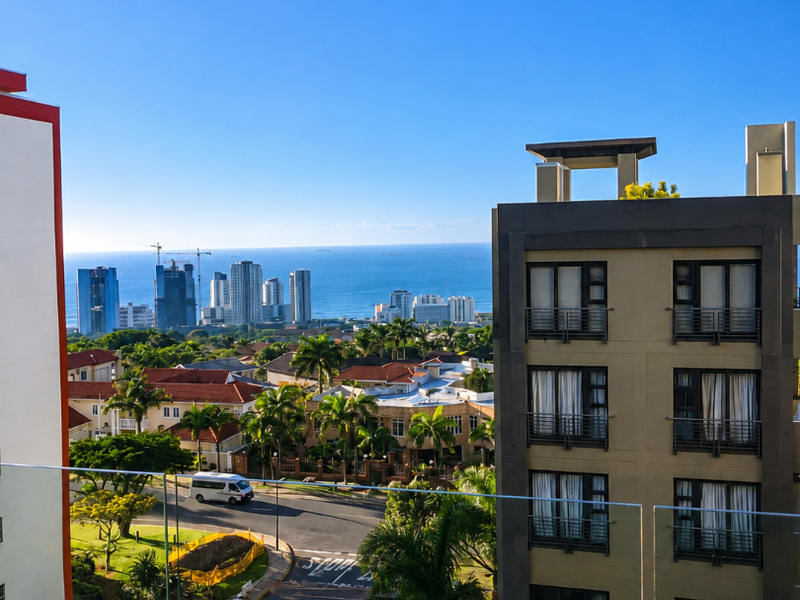 Elevated coastal view overlooking the surrounding neighbourhood, residential buildings, and the ocean horizon, captured from a balcony with a modern glass balustrade.