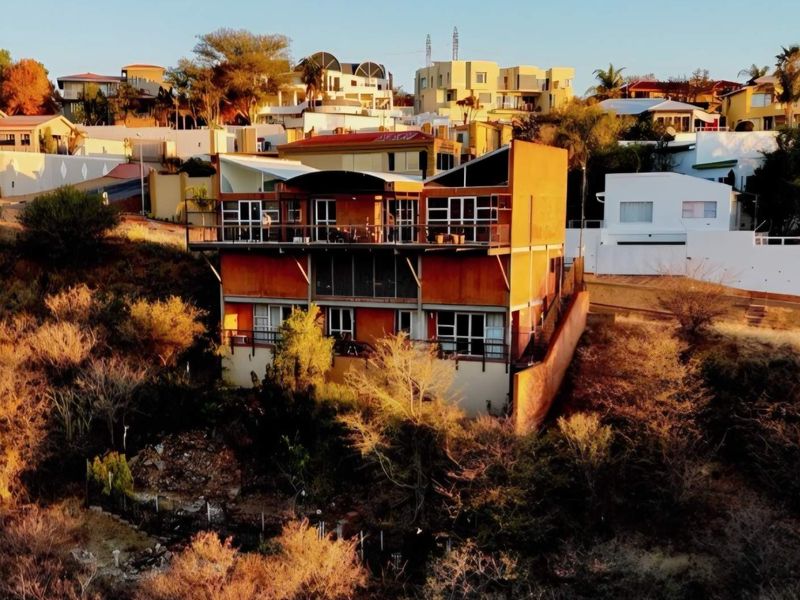 Aerial view of a multi-level residential property featuring tiered balconies and sliding glass doors, situated on a sloped hillside.